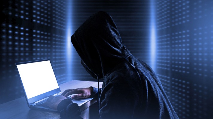 Hacker in a dark room looks into a laptop